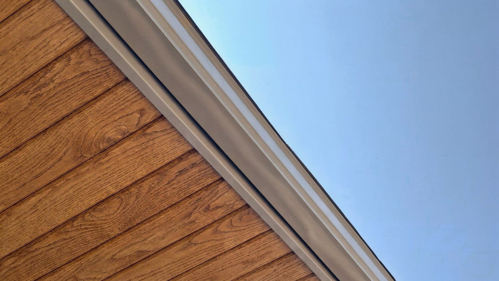 Roof edge with metal gutter and fascia against wood-grain siding and blue sky