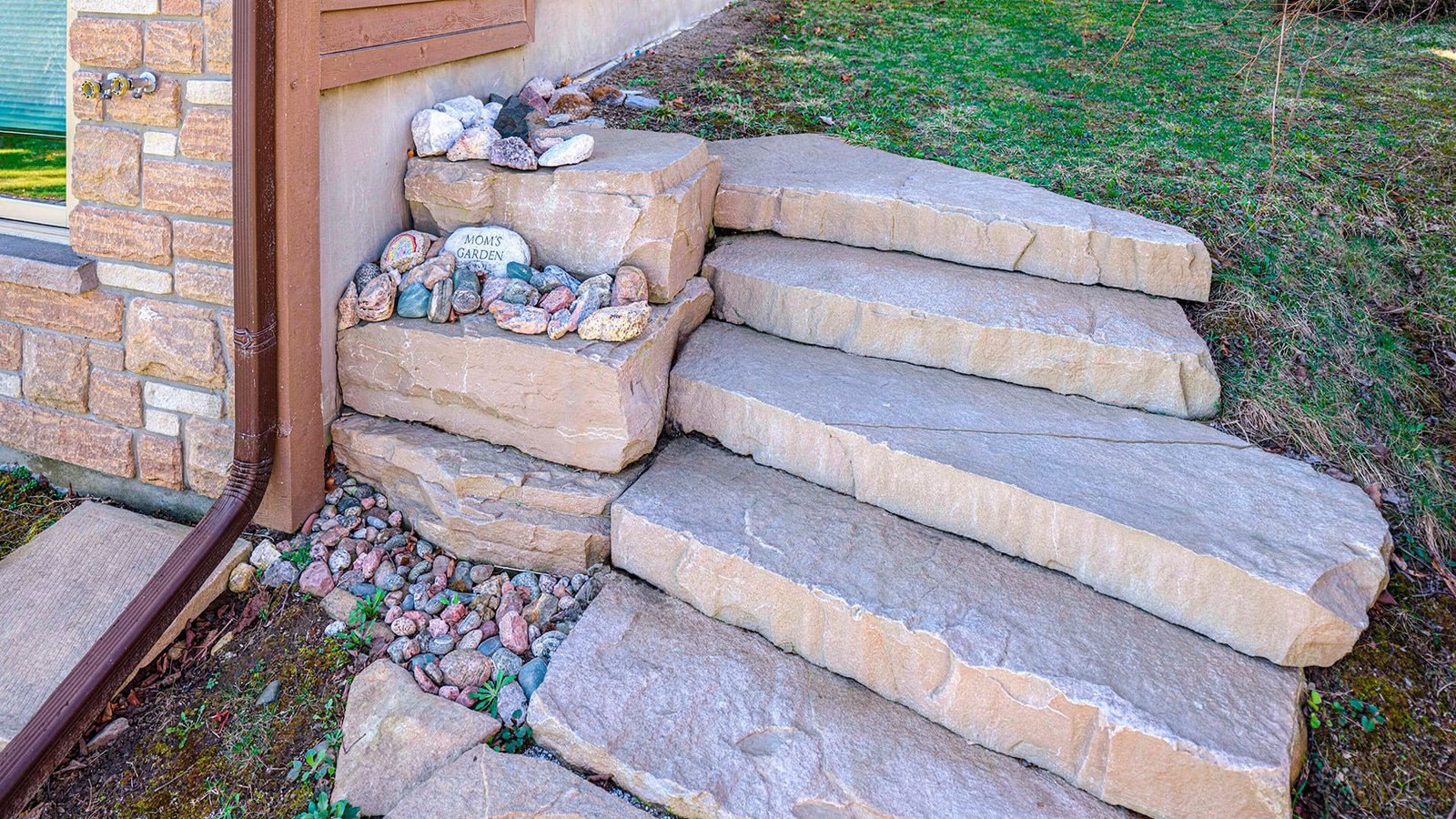 Stone slab steps beside house, with a "Mom's Garden" painted rock and small stone collection at the corner ledge