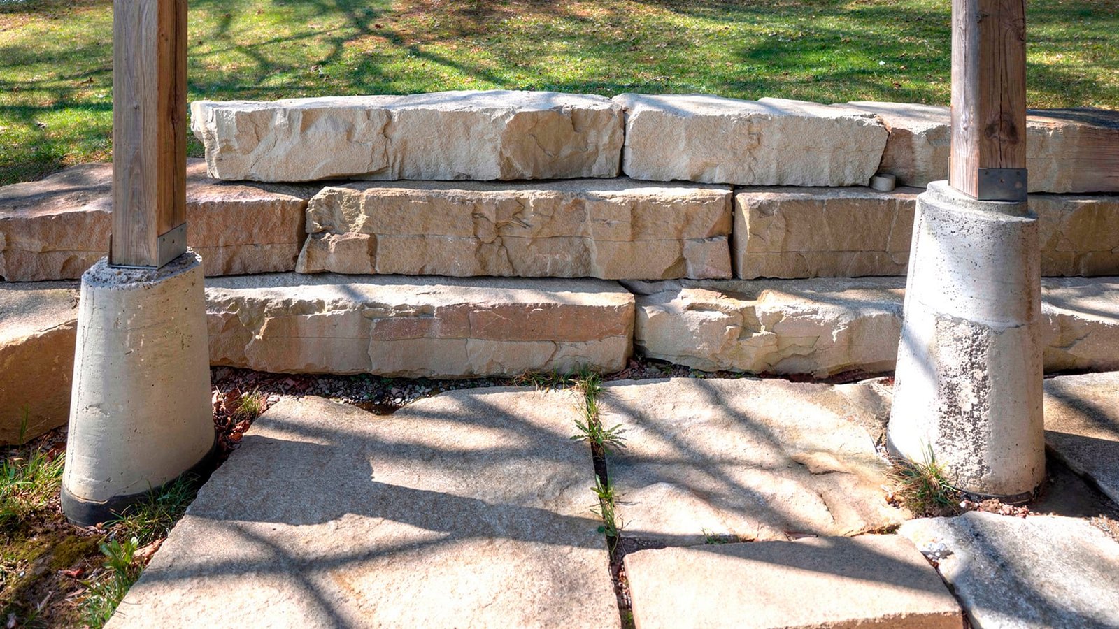 Stacked stone terrace steps with wooden posts on concrete footings and a stone paver patio