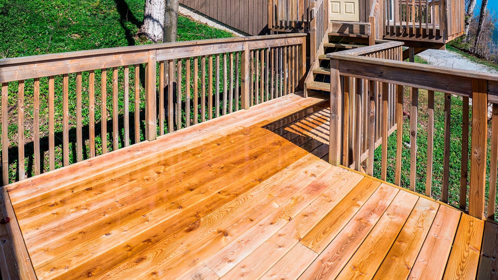 Freshly stained wood deck with railings, stairs leading up to a house, and a green hillside beyond