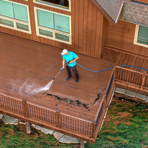 Aerial view of a worker power washing a wooden deck, removing dirt and mildew stains