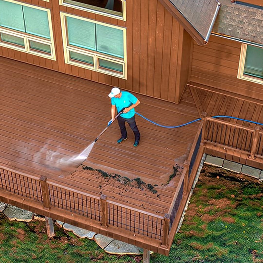 Aerial view of a worker power washing a wooden deck, removing dirt and mildew stains